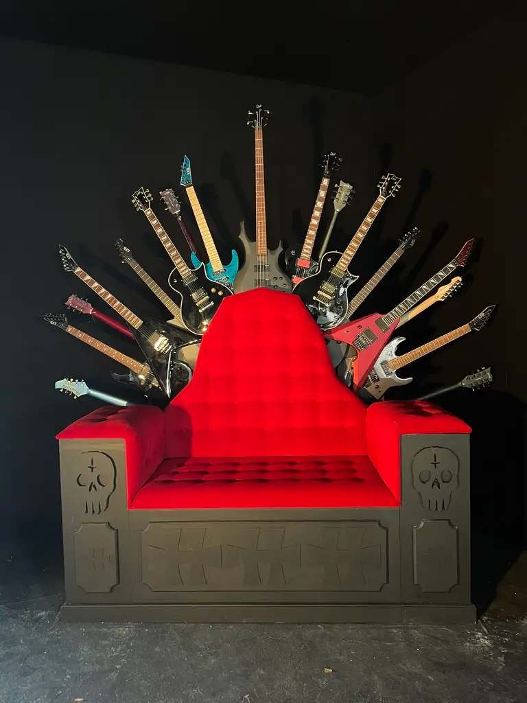 Red velvet throne chair backrest with multiple electric guitars arranged fanning out behind it.