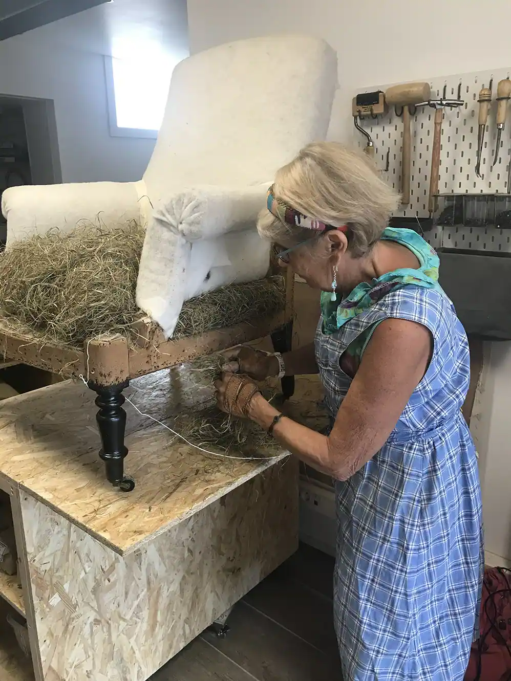Woman upholstering a chair by hand, stuffing it with natural fibers in a workshop.