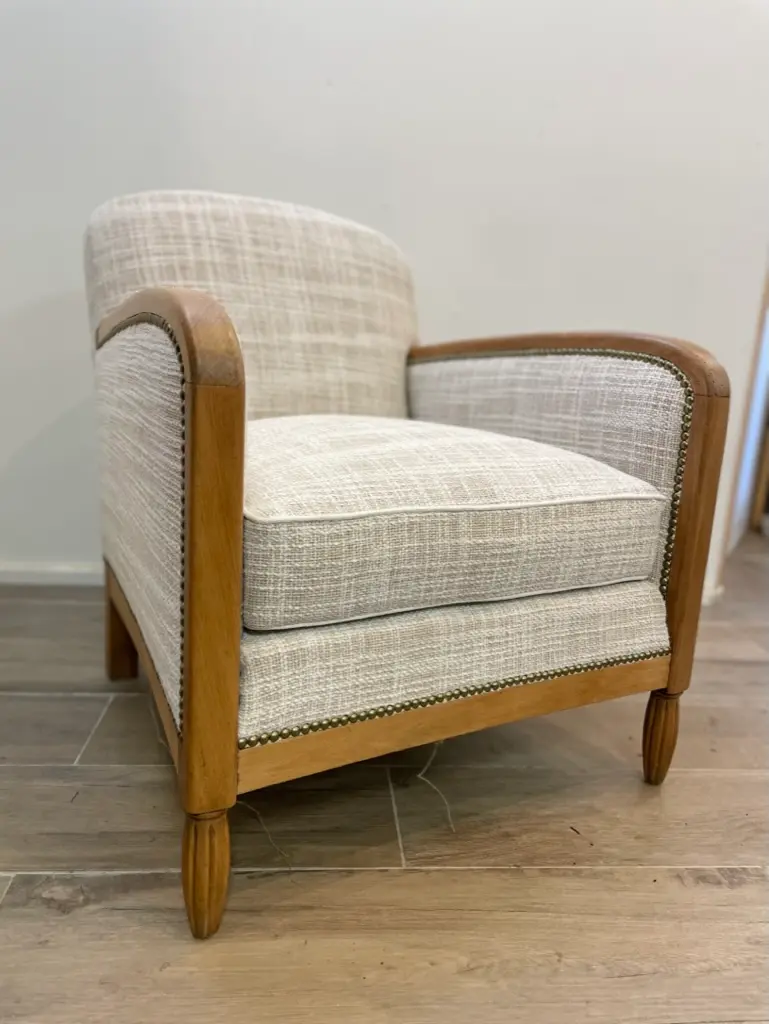 Beige cushioned armchair with wooden frame and carved legs on a wood floor.