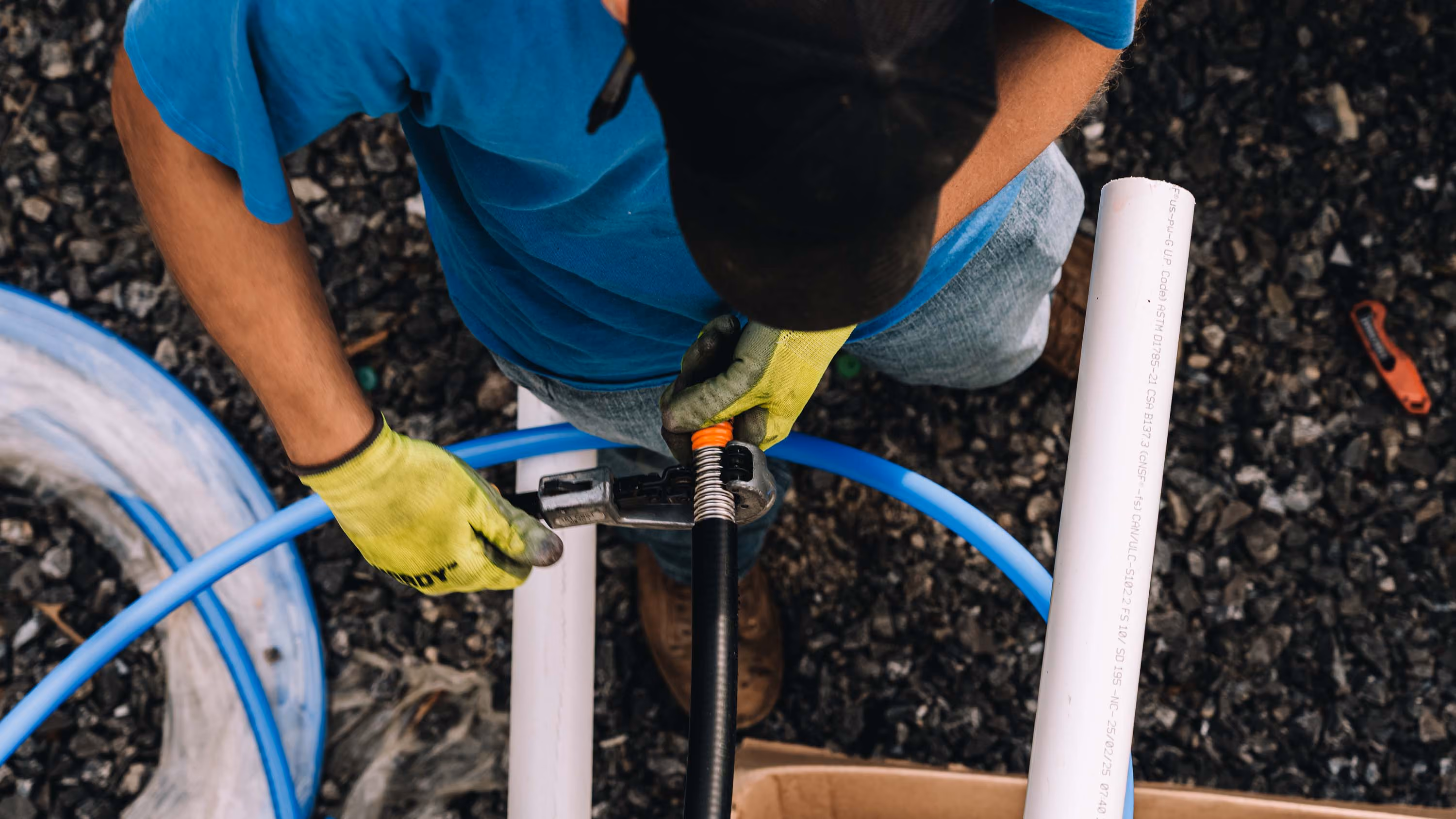 Plumber working on gas lines with blue and white piping in an outdoor setting.