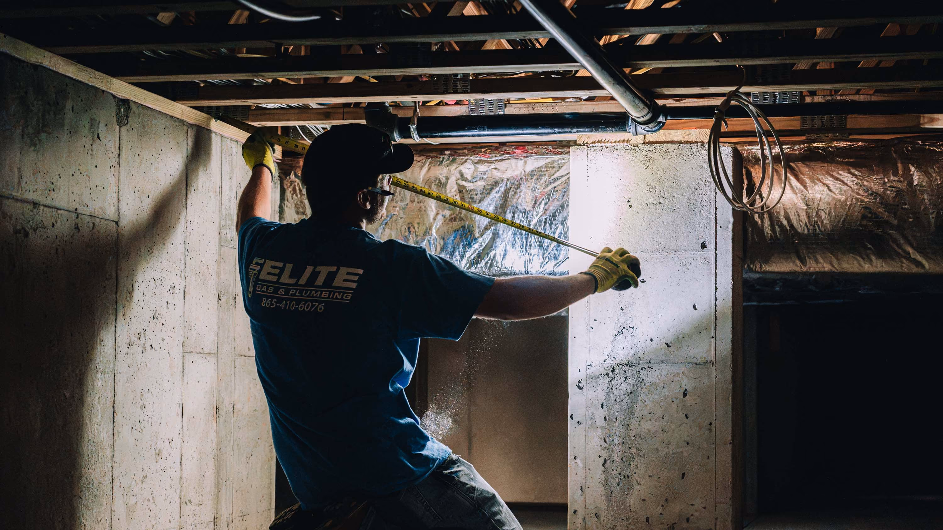 Plumber measures inside a crawlspace during plumbing repairs.