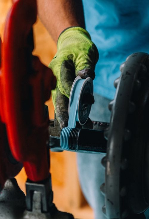 Plumber wearing gloves threads a pipe fitting for plumbing repair.