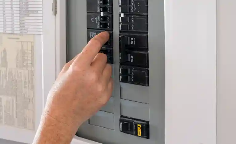 Hand flipping a switch inside an open electrical breaker box, with rows of breakers visible