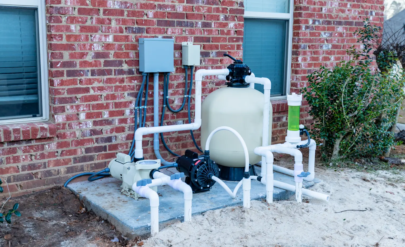 Pool pump and filter equipment outside next to a brick building with nearby plants