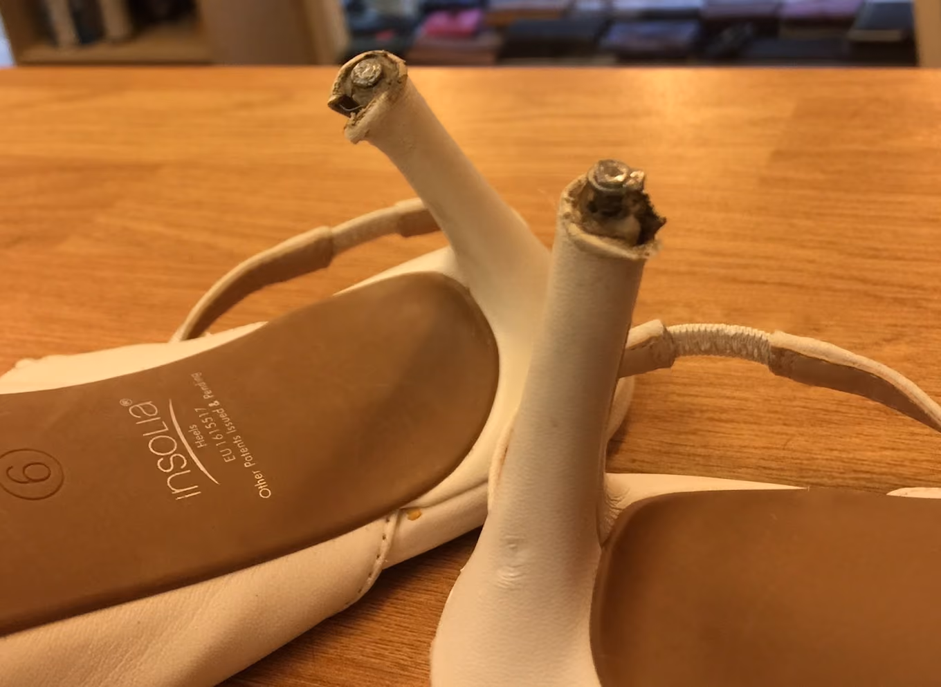Close-up of beige high-heeled shoes with worn-down heels on a wooden surface.
