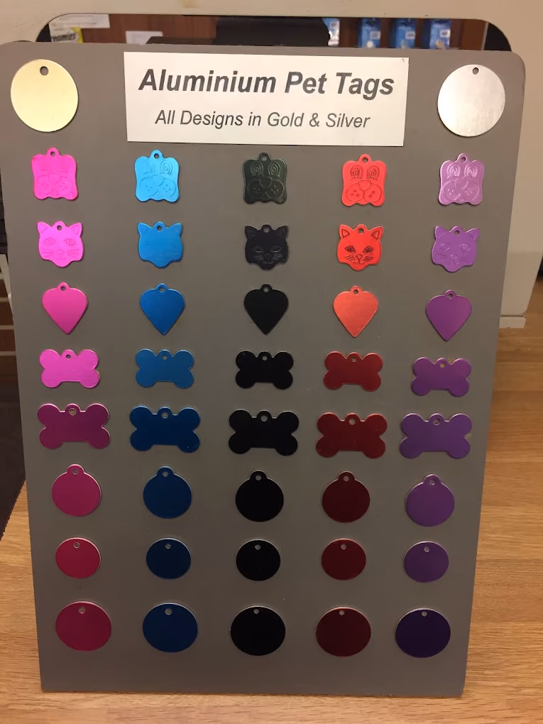 Display board of colorful aluminum pet tags in various shapes like bones, hearts, cats, and paws.