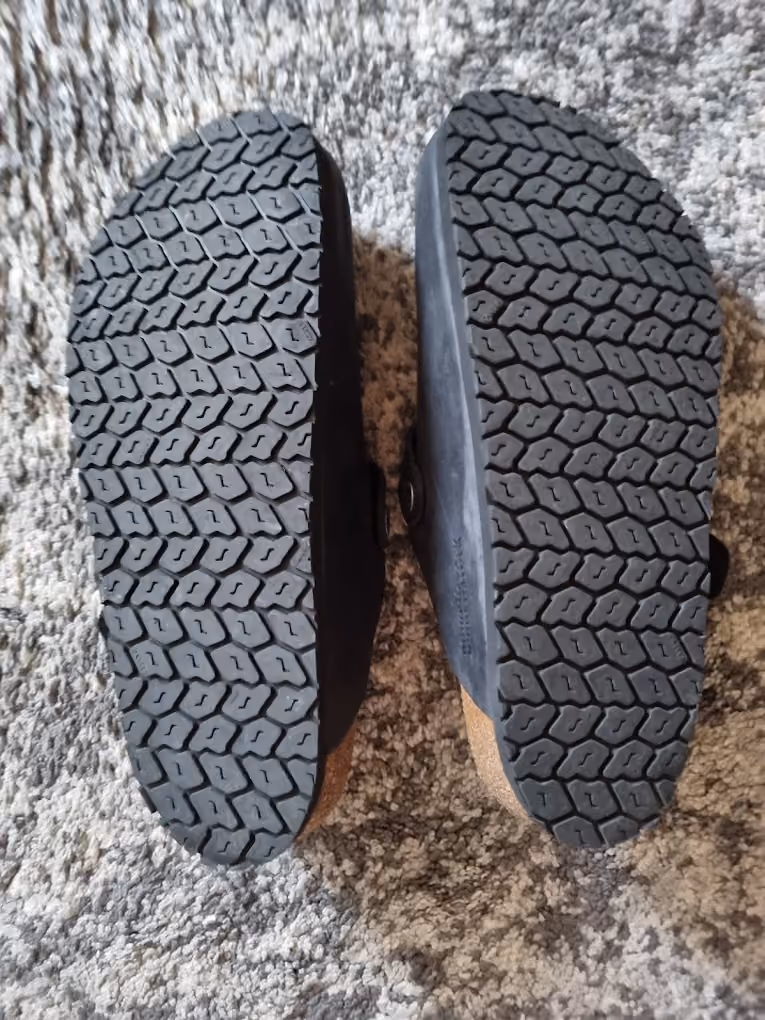 Bottom view of two black-soled shoes with a textured hexagonal tread pattern placed on a carpet.