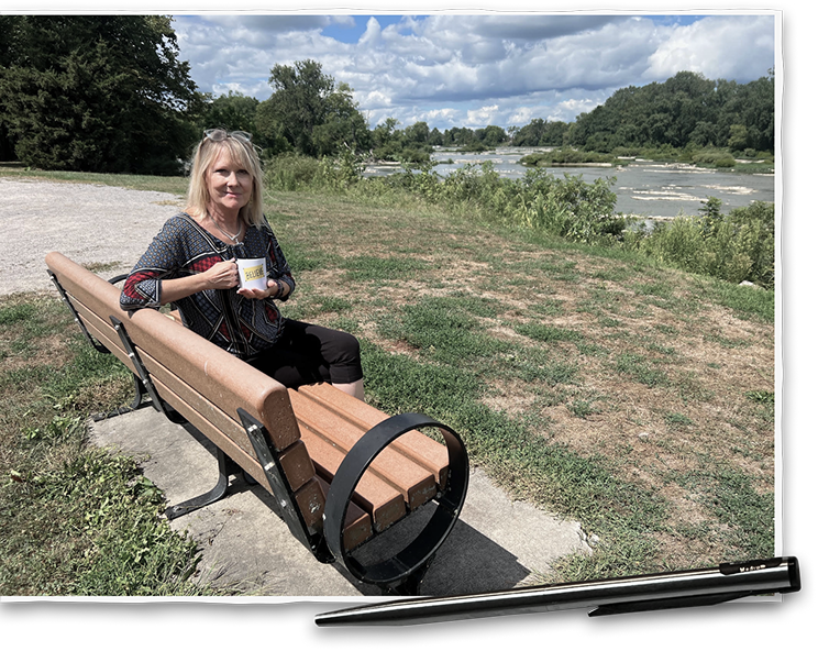 Author Carole Sarkan sitting on a bench overlooking the Maumee river