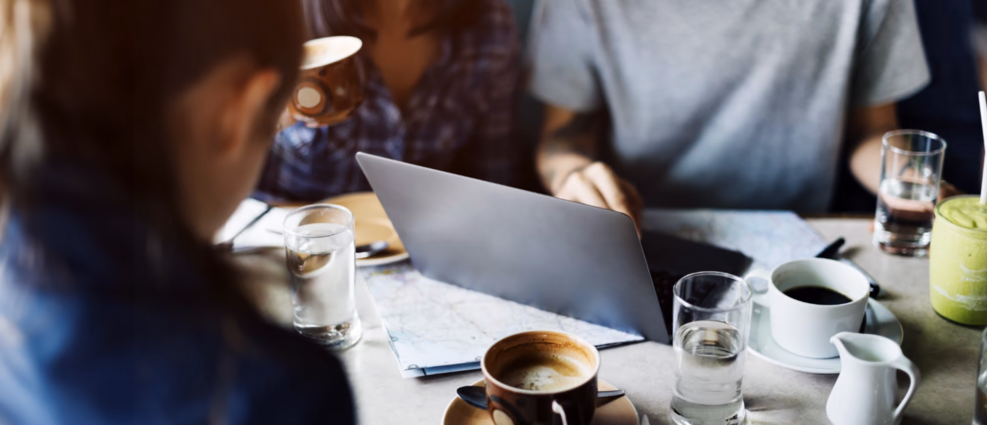 People in a cafe with a laptop in the middle and coffee around
