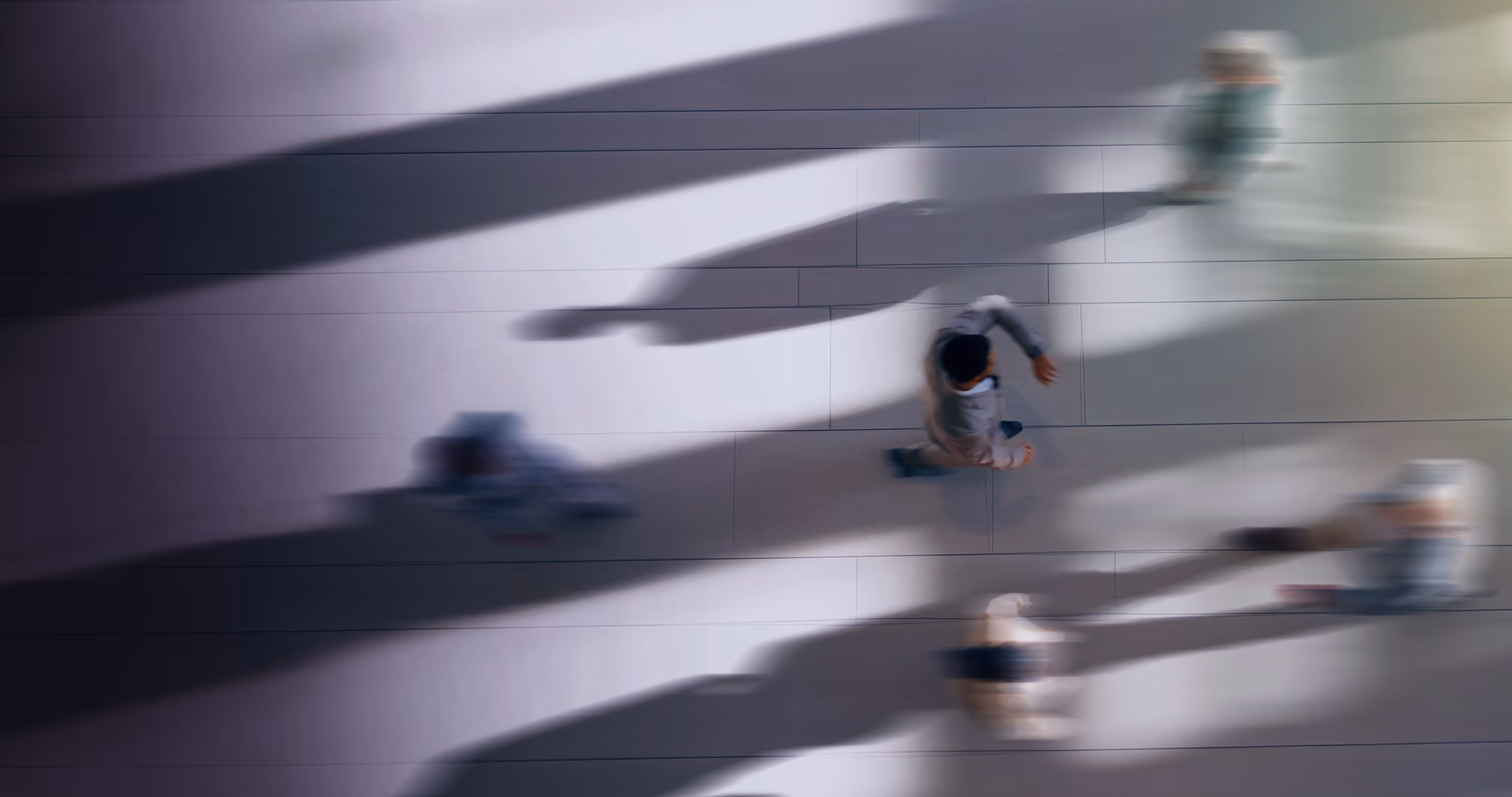 Blurred overhead view of people walking on tiled floor with long shadows.