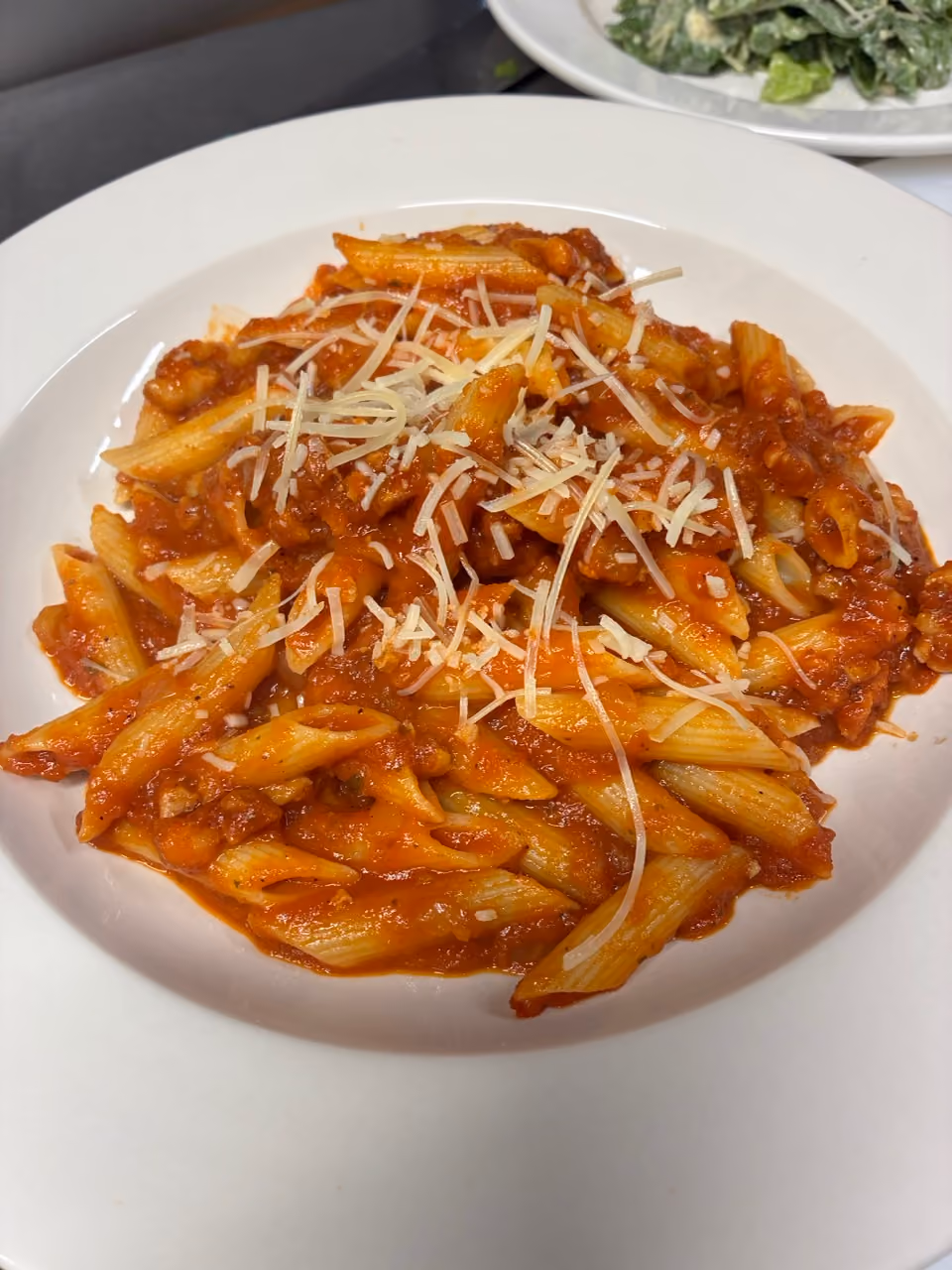 Plate of penne pasta with tomato sauce and shredded cheese on top.