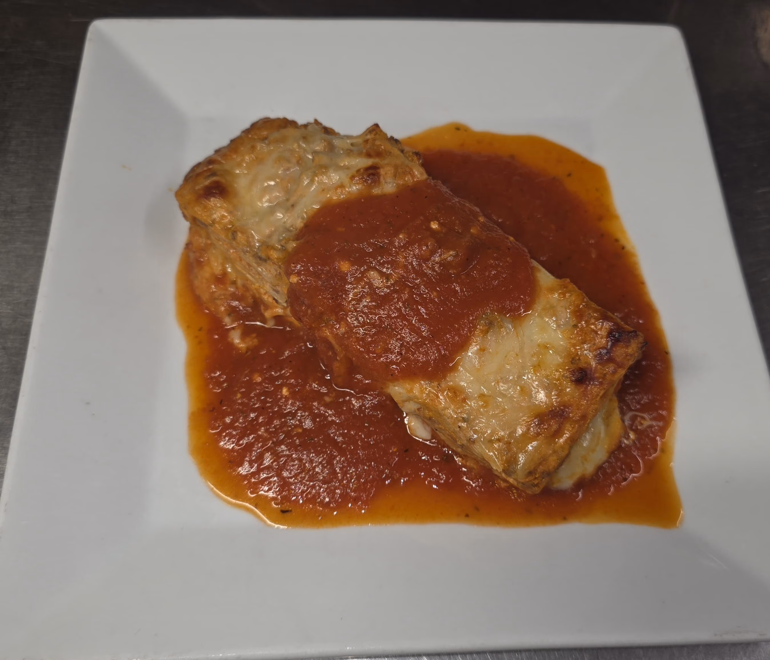 Baked lasagna square with melted cheese and tomato sauce on a white square plate.