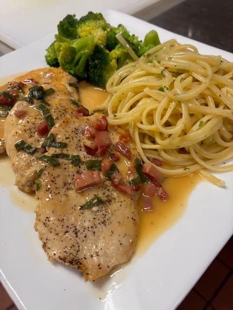 Plate with two cooked chicken breasts in sauce, spaghetti, and steamed broccoli.
