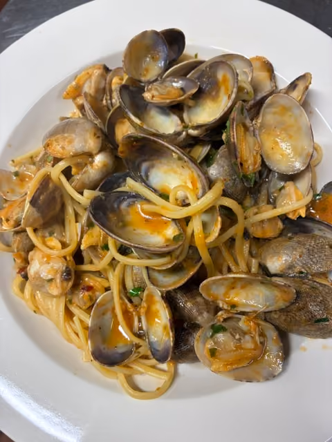 Plate of spaghetti pasta with cooked clams in a light sauce garnished with herbs.