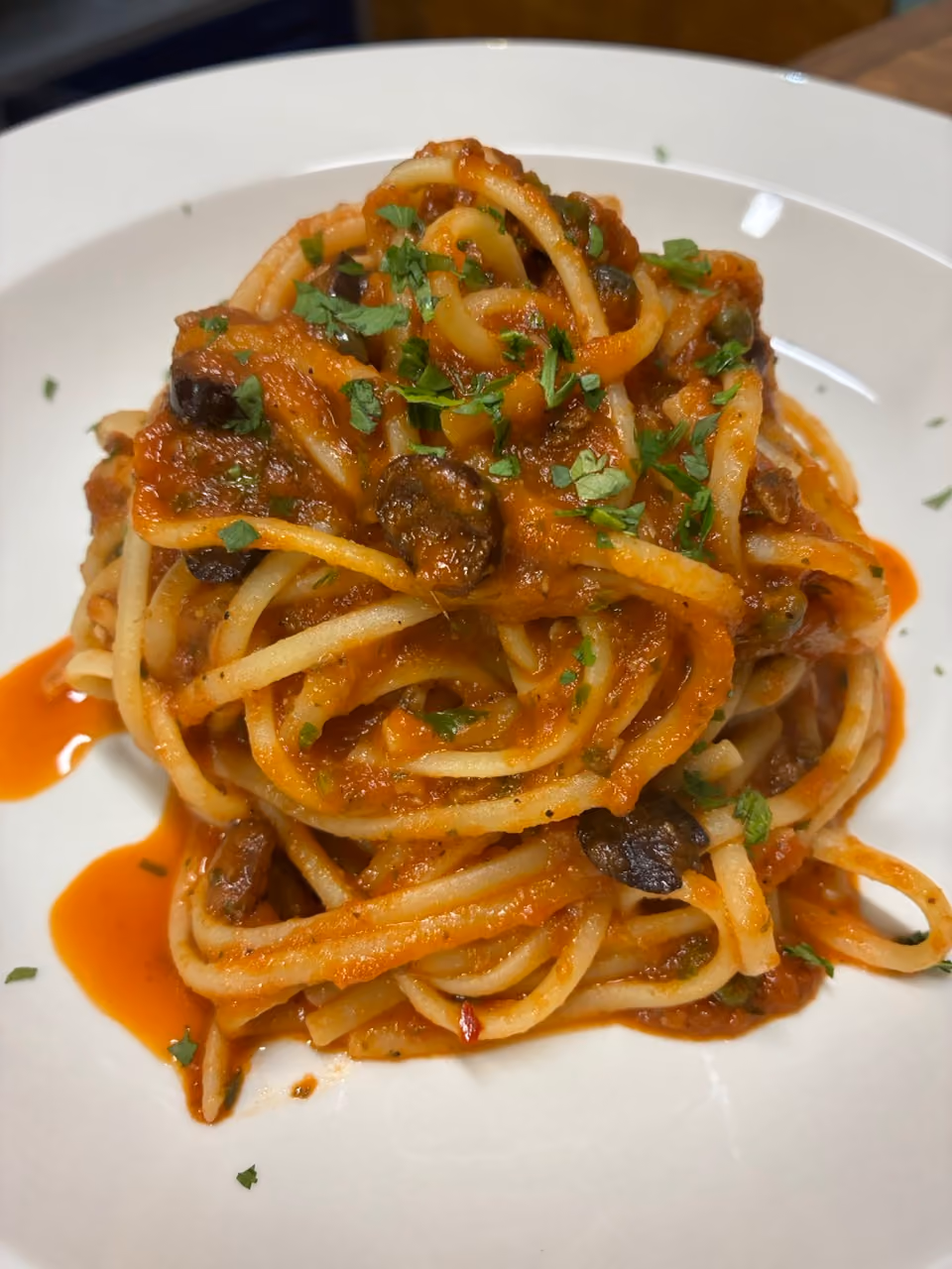 Plate of spaghetti with tomato sauce, olives, and chopped parsley on top.