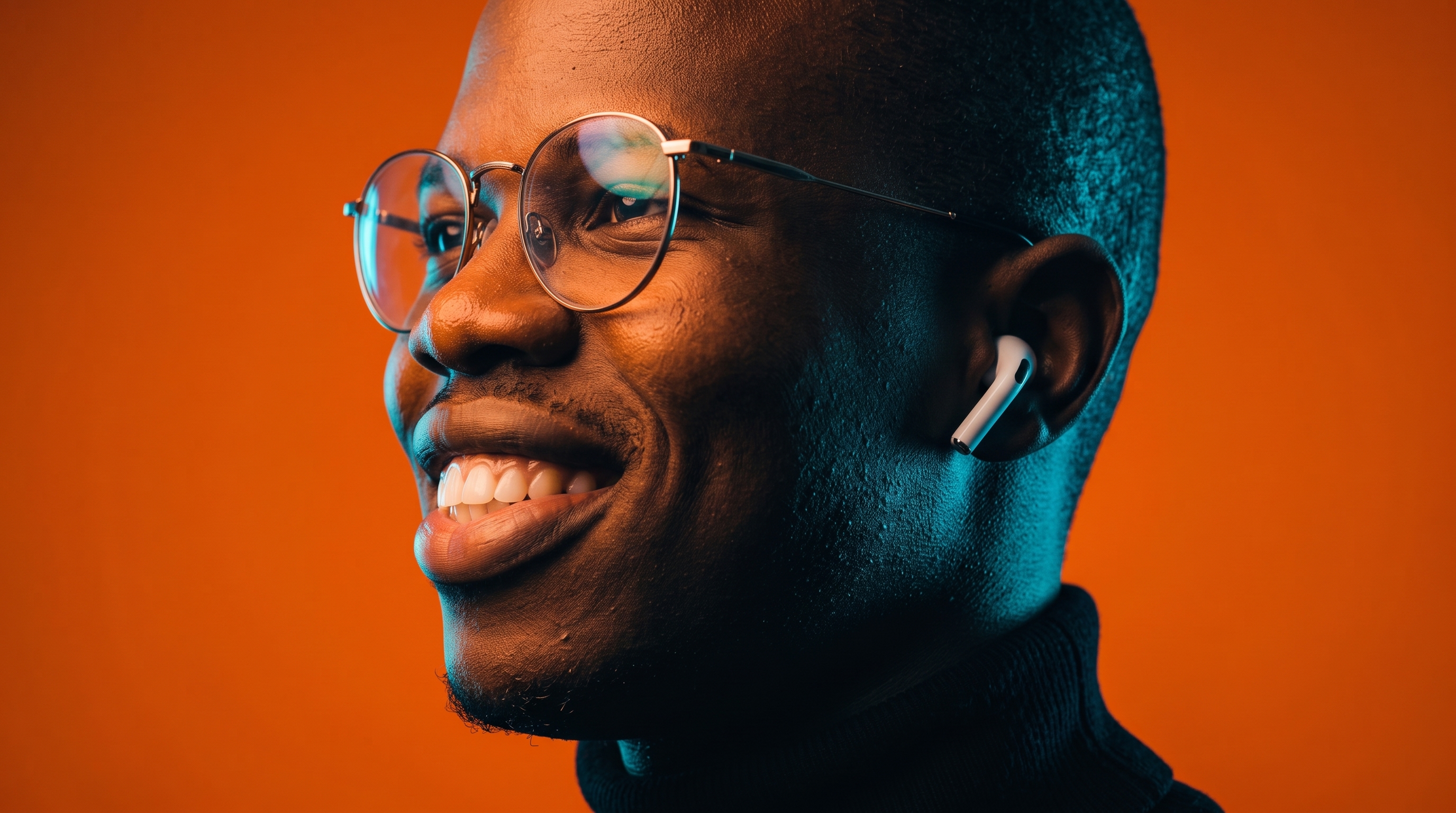 Smiling man wearing glasses and white wireless earbuds against an orange background.