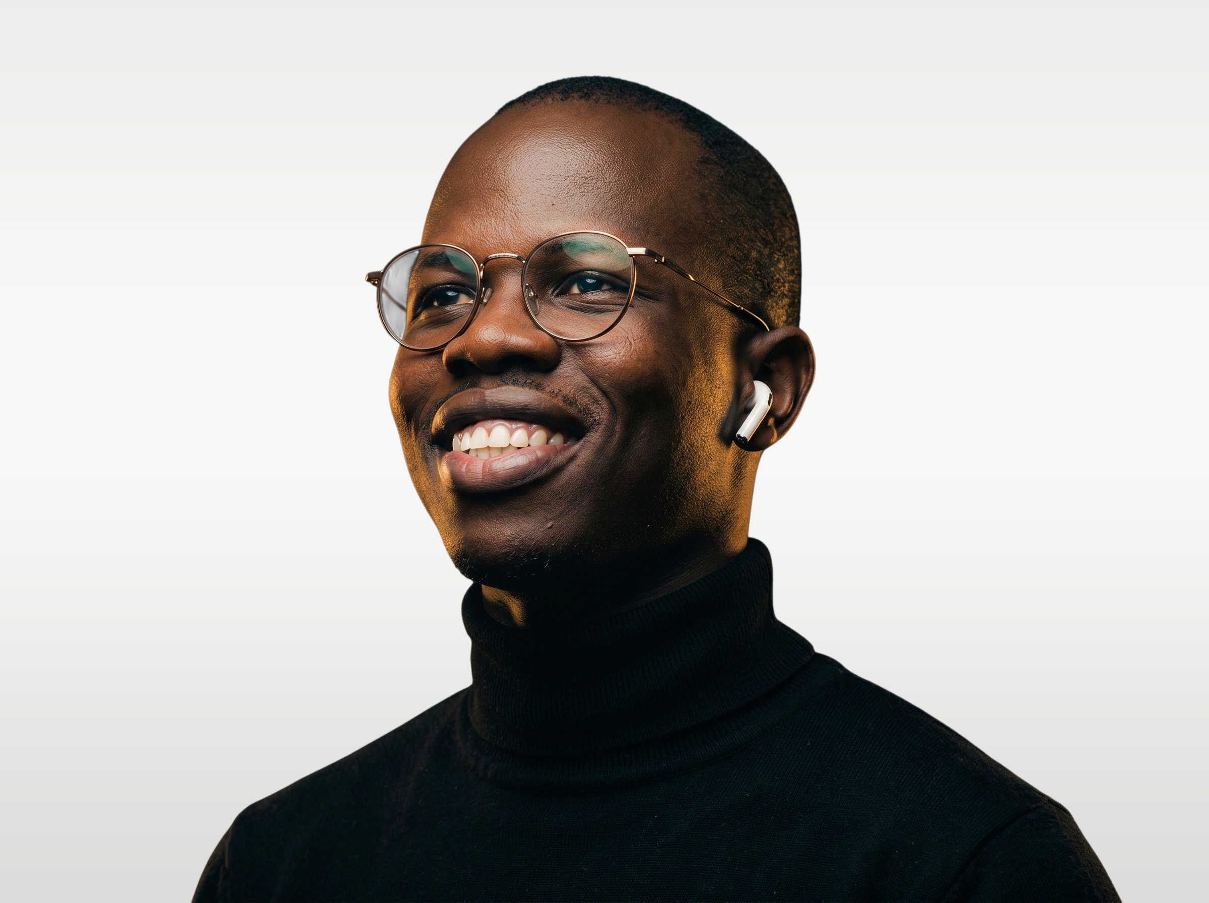 Smiling man with round glasses and wireless earbuds wearing a black turtleneck on a light background.
