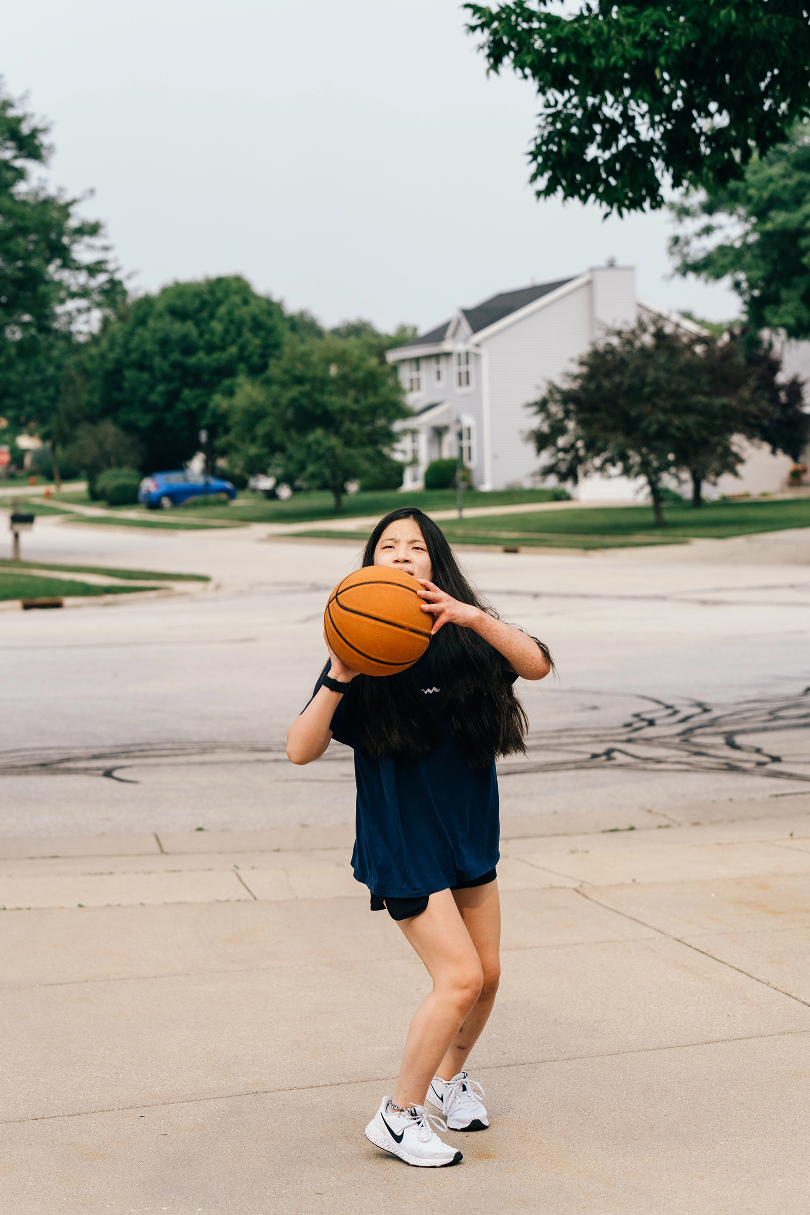 Girl in navy shirt and shorts preparing to shoot a basketball outdoors on a driveway.