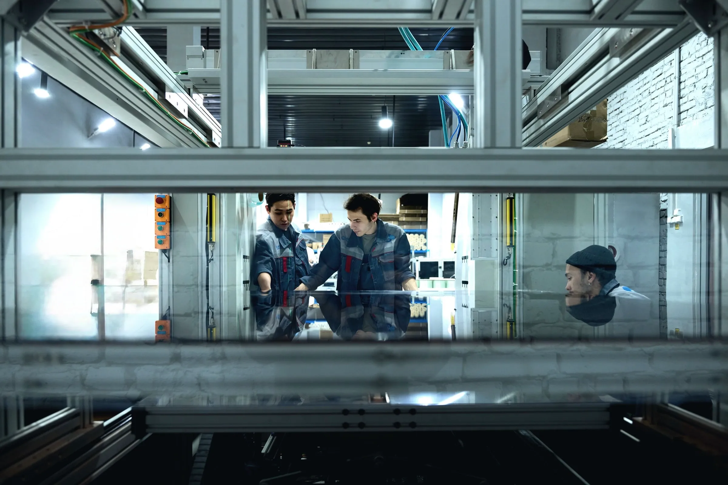 Two workers conferring over a panel behind a glass partition