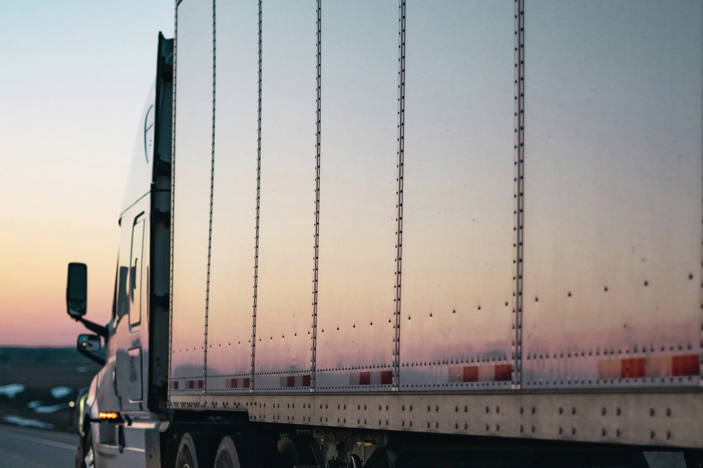 A tractor trailer running on the road at dusk