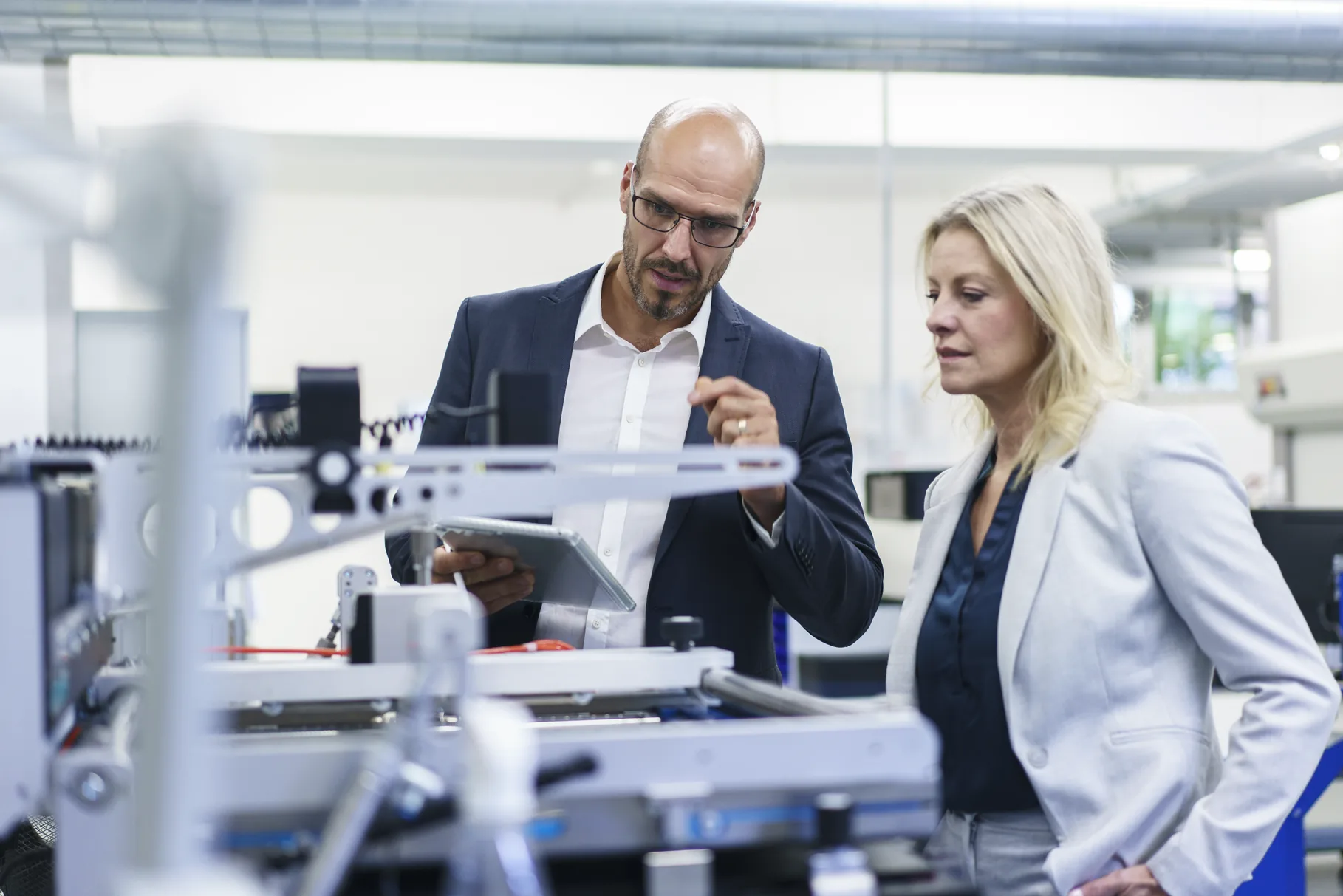 Two people talking over a tablet beside a machine on a factory floor