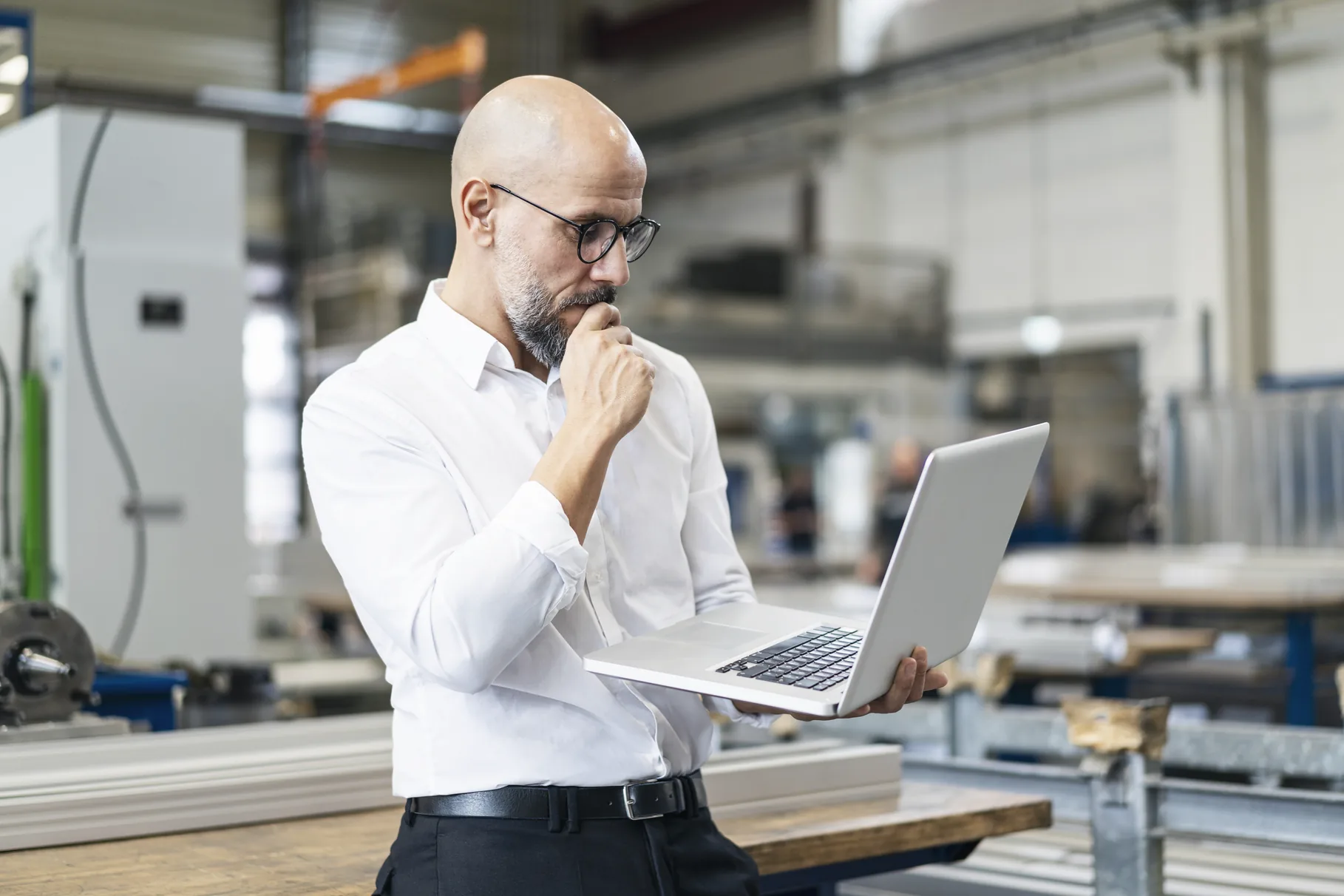 A manager standing in a machine shop reading something on a laptop