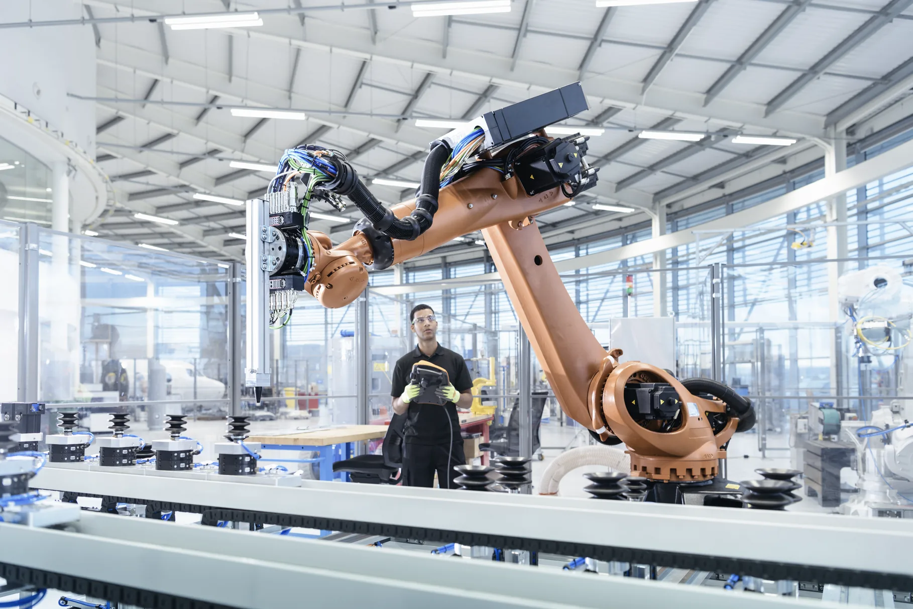 An engineer holding a teach pendant beside a robot arm on a production line