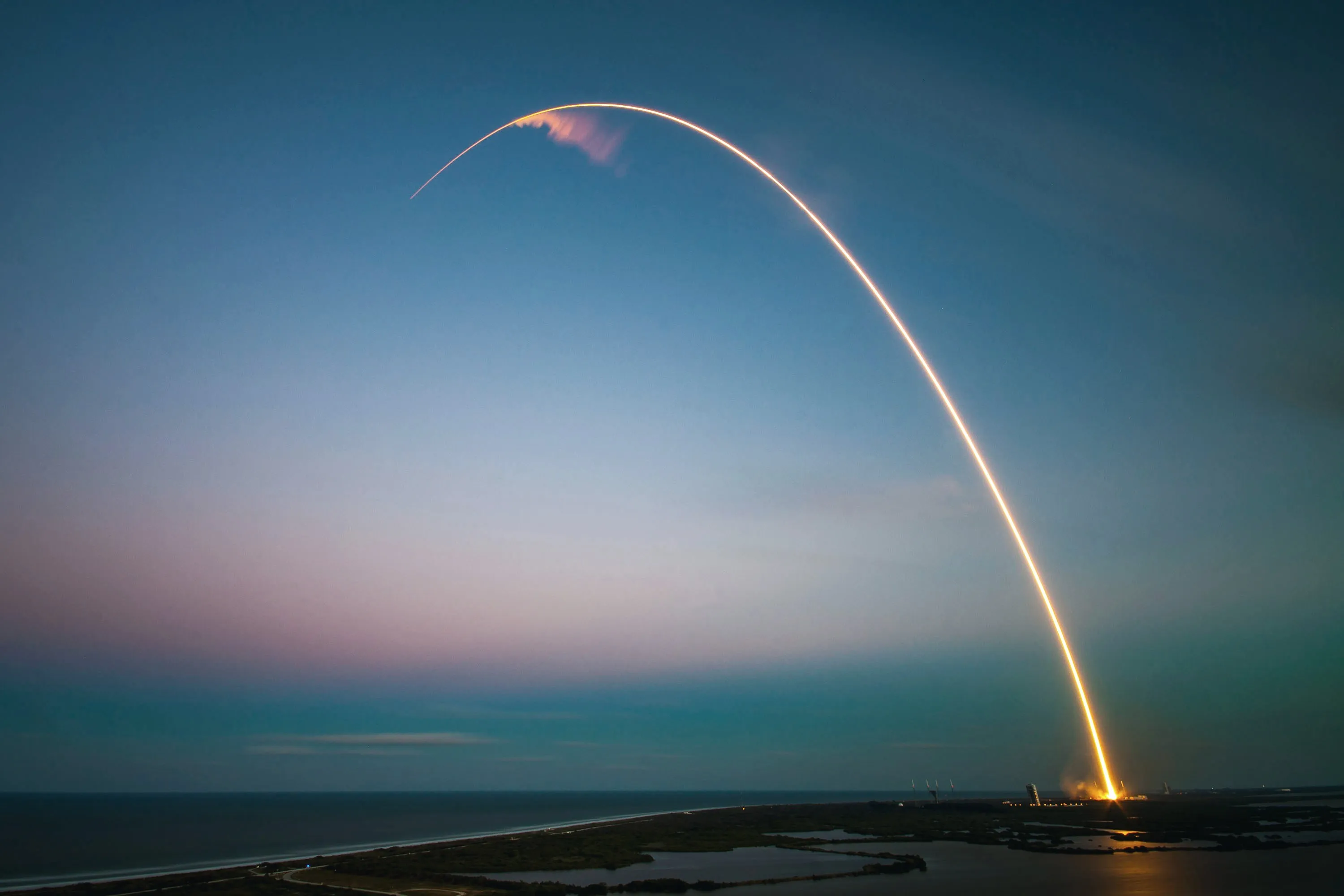 A launch trail arcing over the coast at dusk