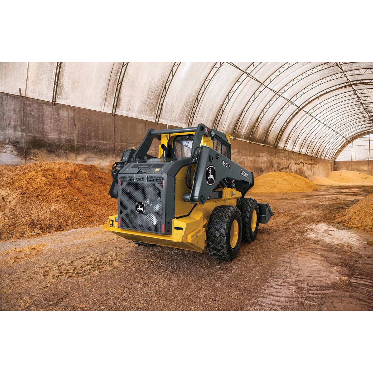 330 P skid steer loader in black and yellow is parked inside a large arched storage building with a translucent roof.