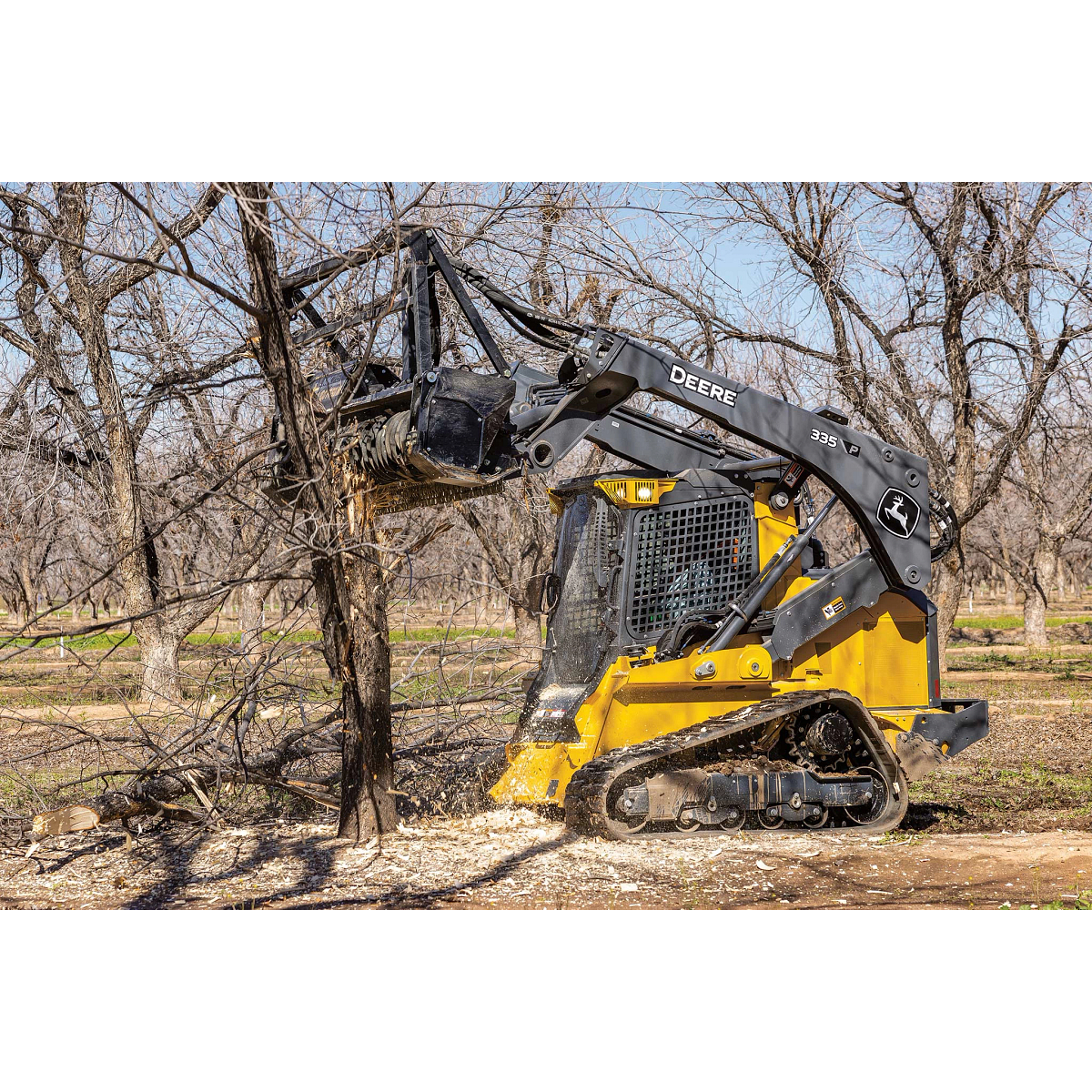 Side left view of a 335 P-Tier compact track loader grinding a tree with an MK76 mulching head