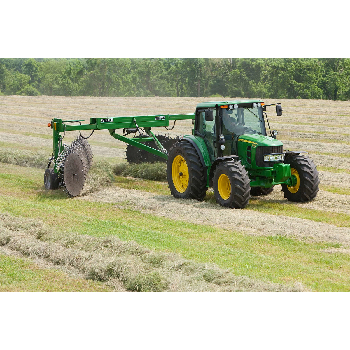 Front right view of a tractor and WR5417 wheel rake at work on windrows in a tree-lined hay field