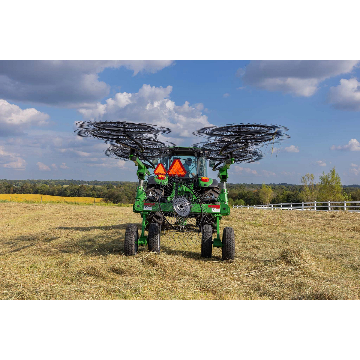 Rear view of a 5125M tractor in a hay field with WR3210 wheel rake folded into transport mode