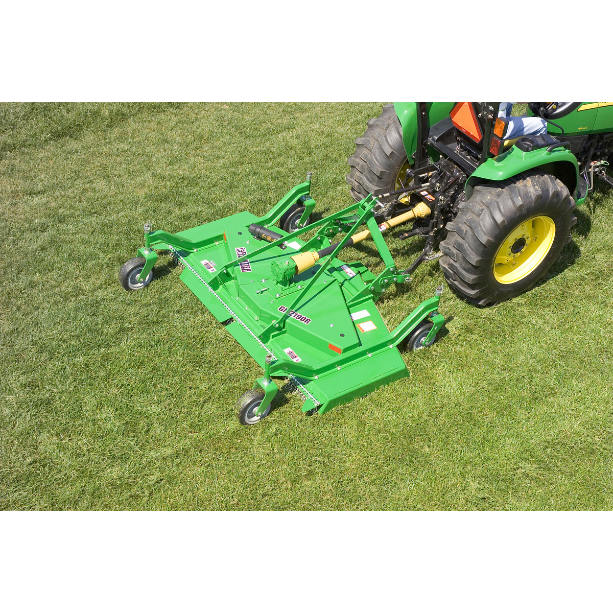 Aerial right view of a green Frontier GM2190R grooming mower on grass with the back end of attached compact tractor in the top right of the image.