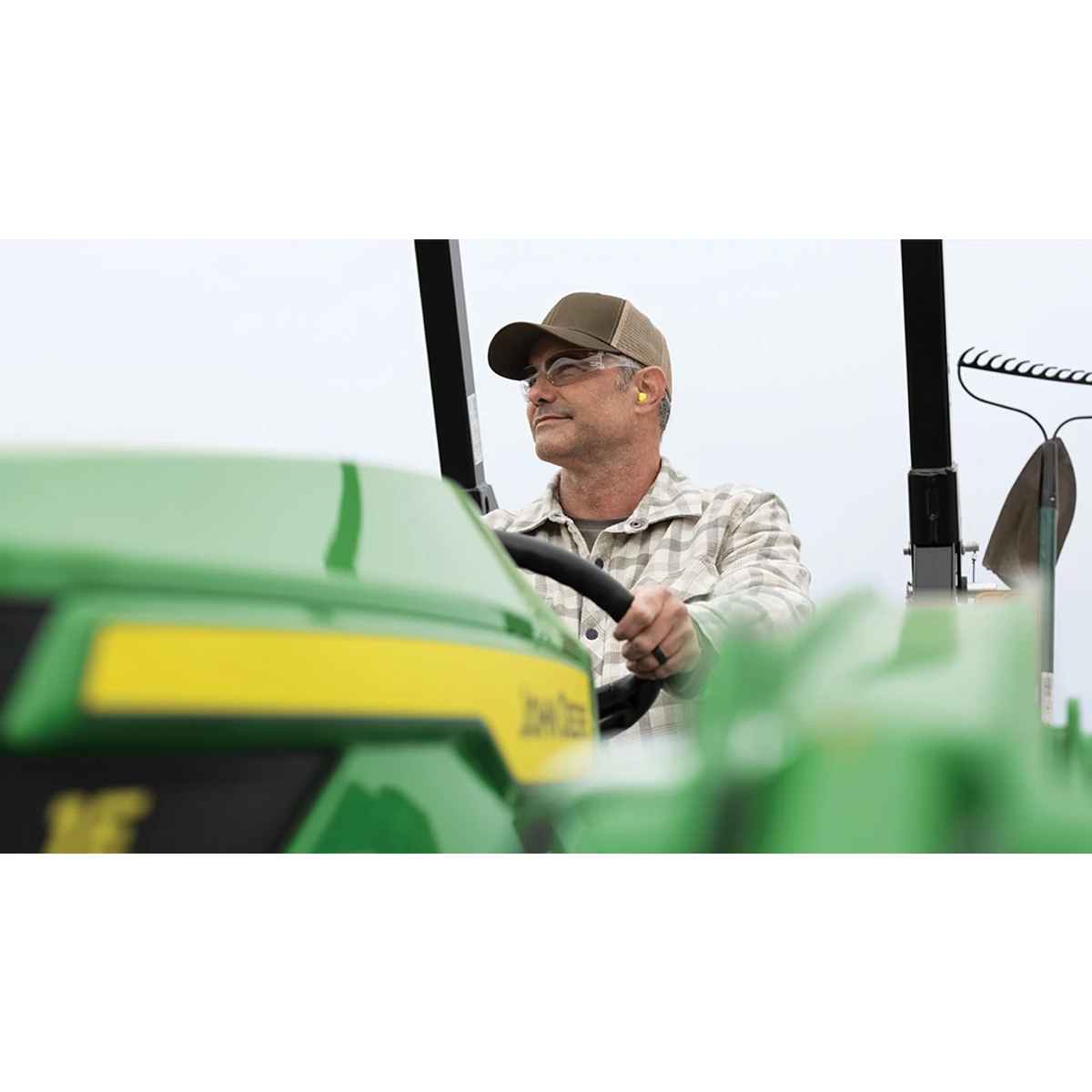 Close up of a person smiling atop an out-of-focus green compact tractor.