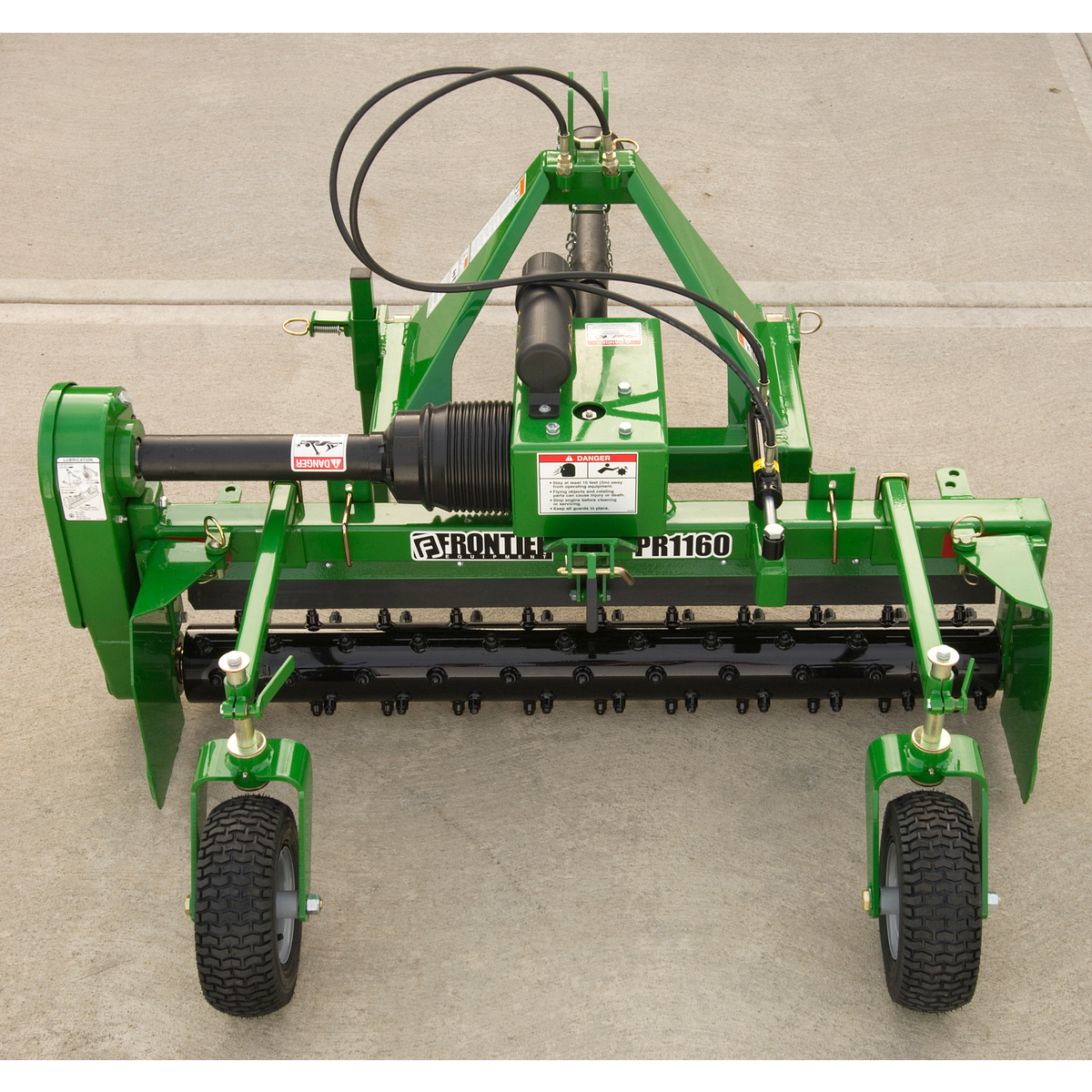 Front view of a green Frontier PR1160 agricultural implement with a steel frame, hydraulic hoses, rotating cutting drum, adjustable side skids, and two black rubber support wheels on a concrete surface.