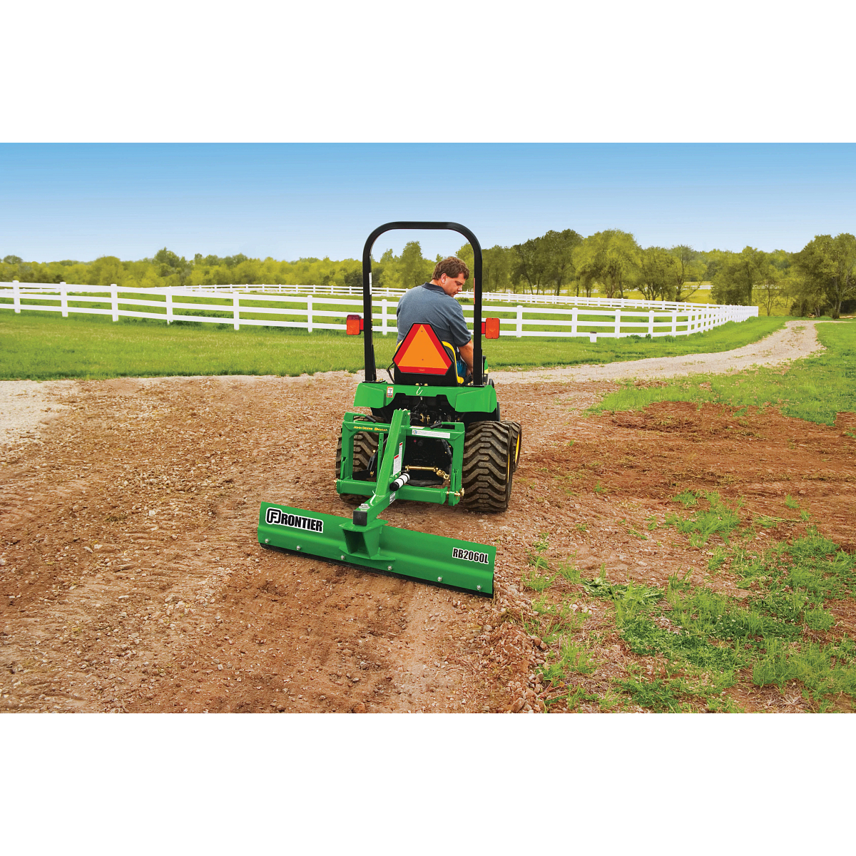 Rear view of a tractor on a farm path using a green, rear-attached RB2060L Rear Blade