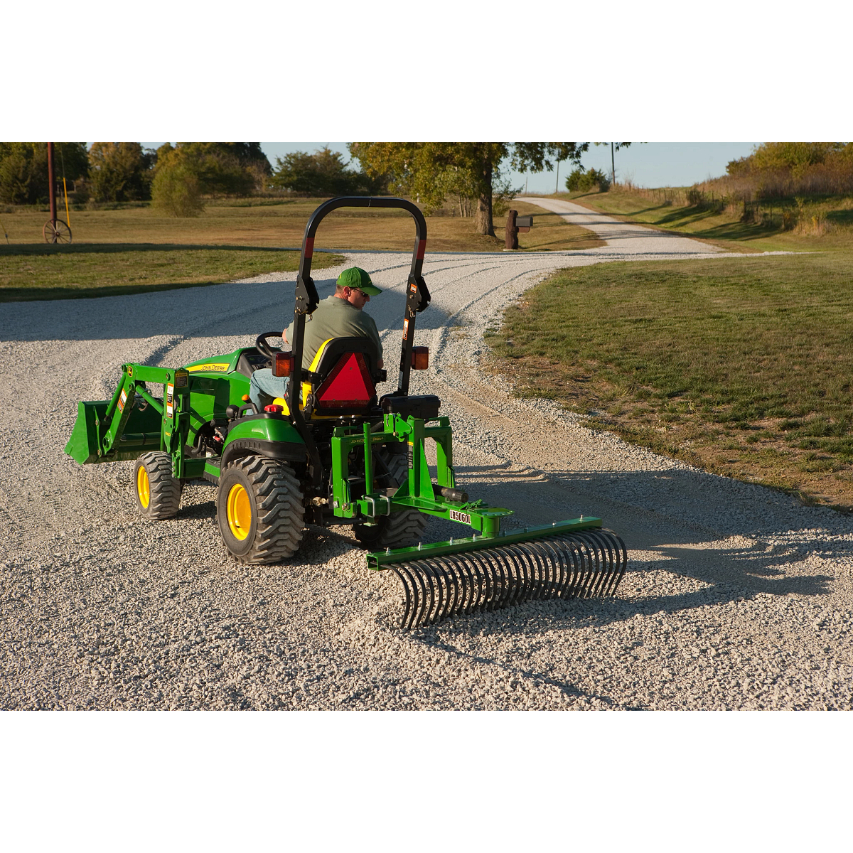 Man drives tractor pulling a landscape rake on a road
