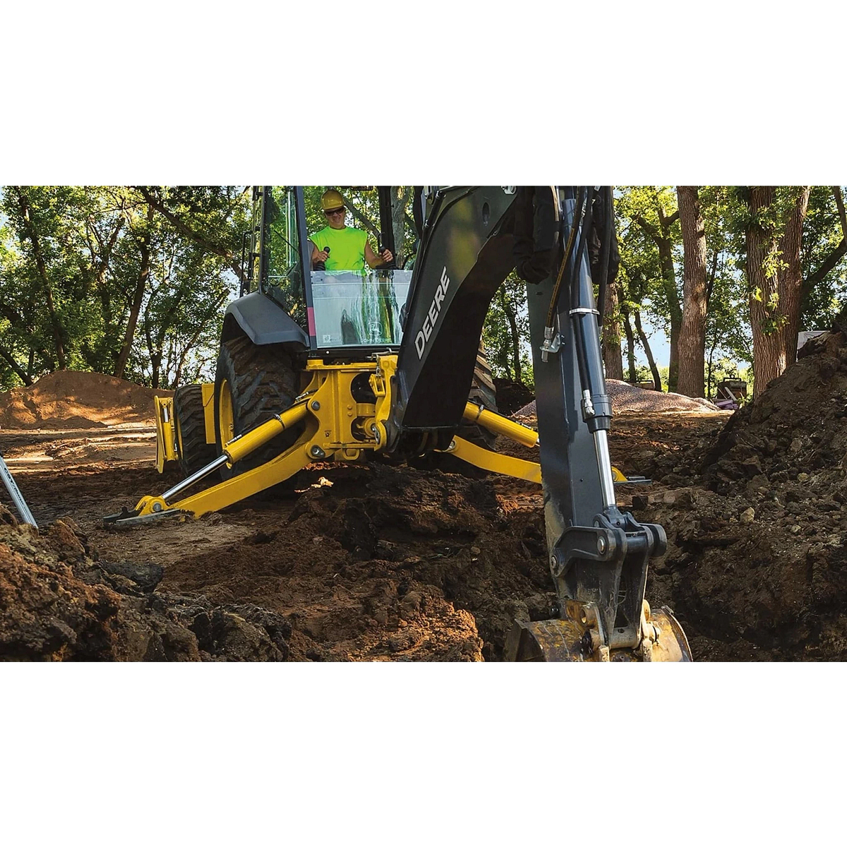 An operator digging a hole in a wooded area with a 710 P-Tier Backhoe