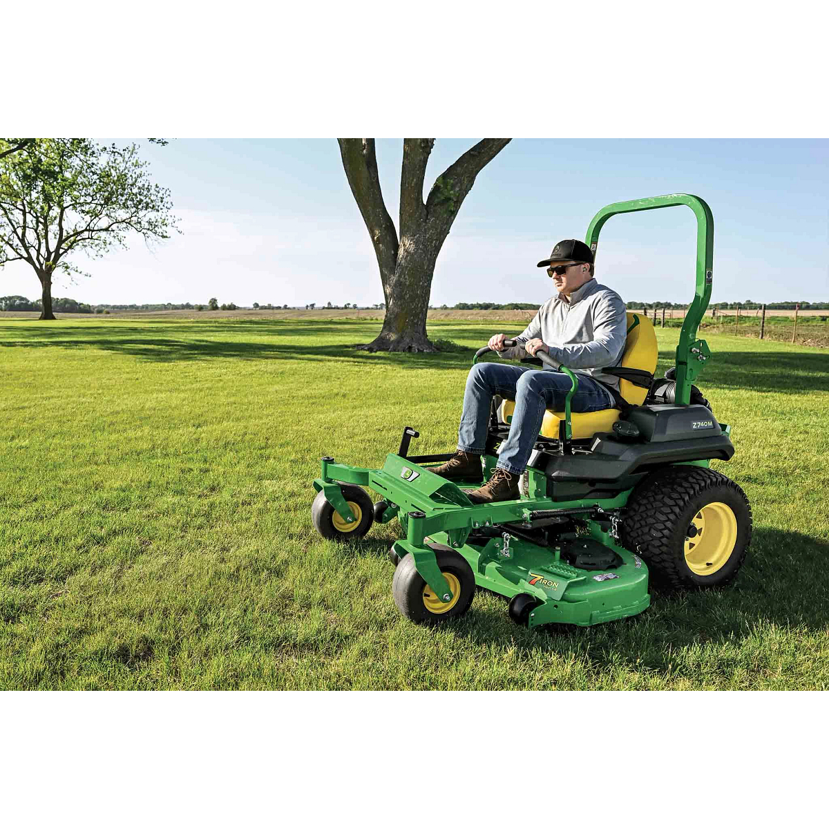 A green zero-turn mower being used to tend a large wide-open field.