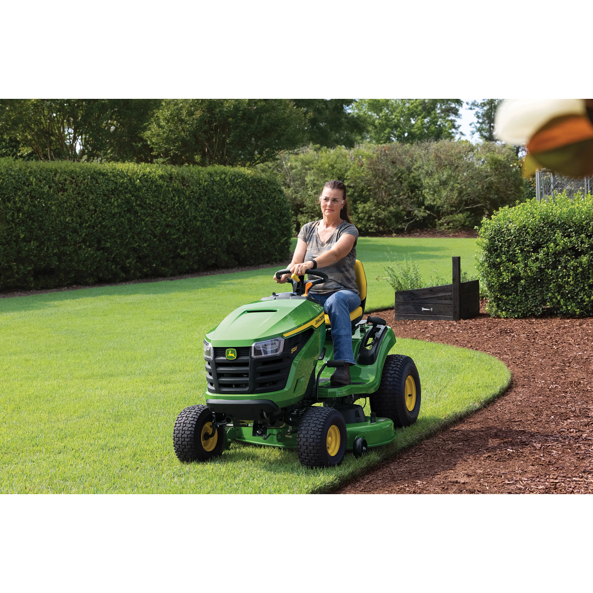 Homeowner driving an S120 Lawn Tractor along a landscaped lawn