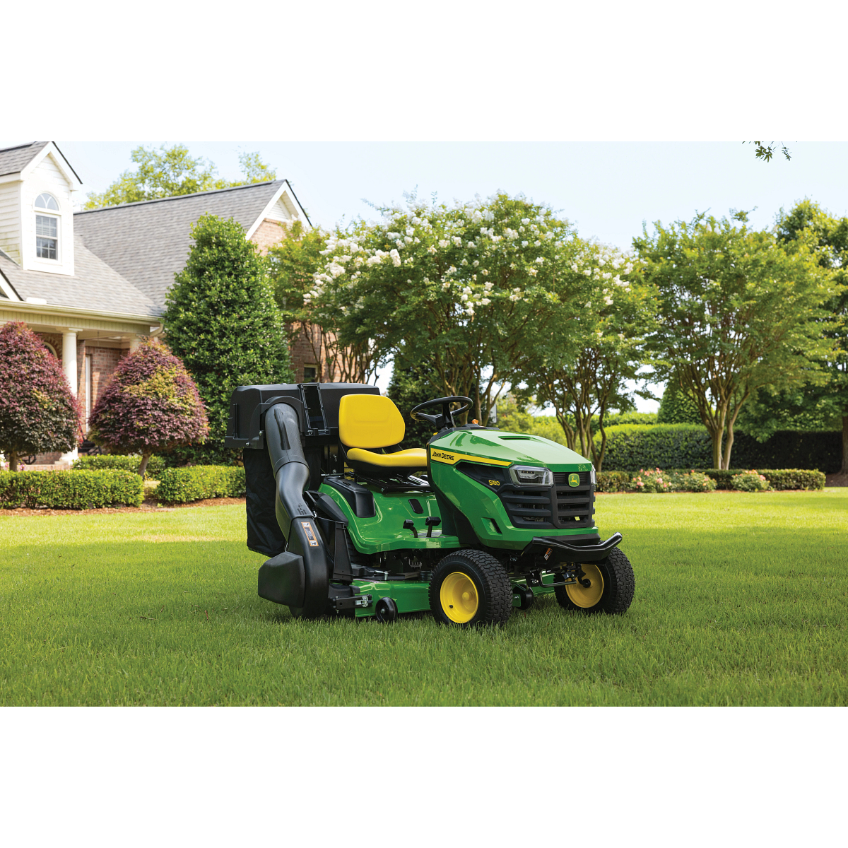 Front right view on an S180 Lawn Tractor with attached material collection system in the middle of a residential lawn