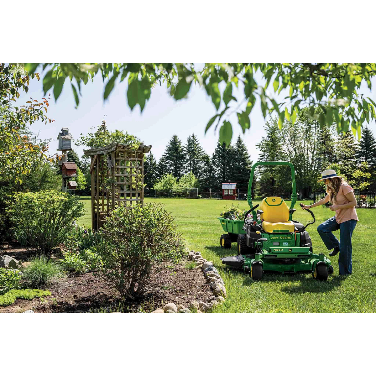 A person steps onto a zero-turn mower with a poly cart attachment hauling plants.