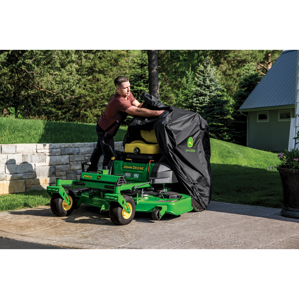 A cover with the Deere logo being removed from a green zero-turn mower in a driveway.