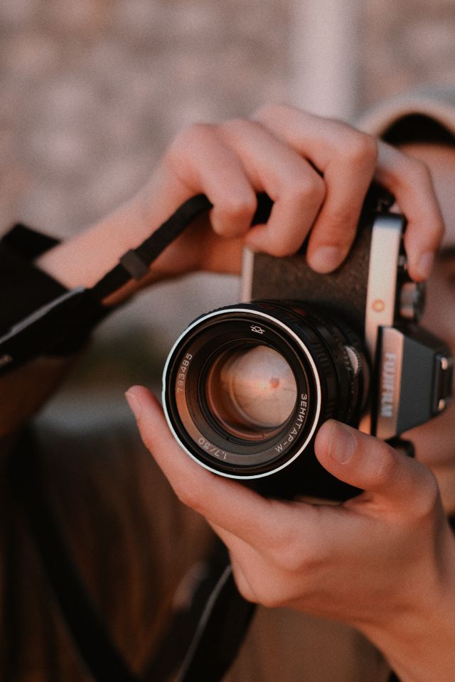 Close-up of hands holding a vintage camera with a large lens, focusing on the lens details and grip.