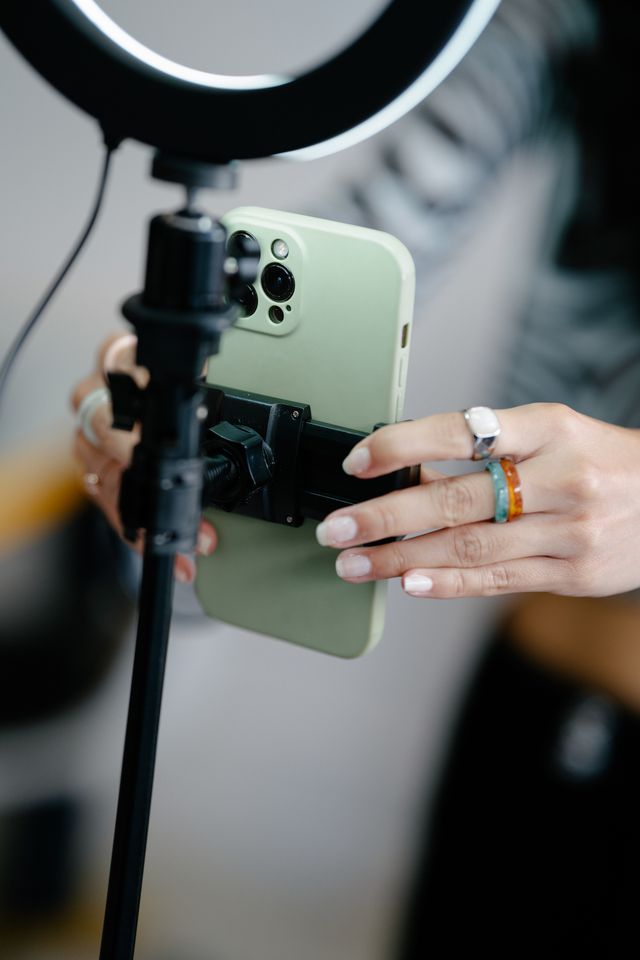 Close-up of hands adjusting a green smartphone mounted on a holder attached to a tripod stand with a ring light above.