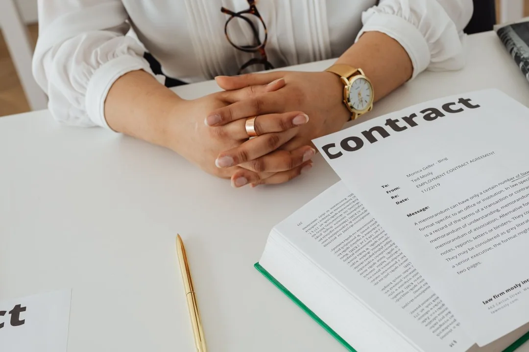 A person seated at a desk with an open contract document and reading glasses