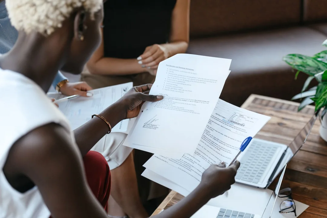 Two colleagues at a table comparing one document against a set of papers