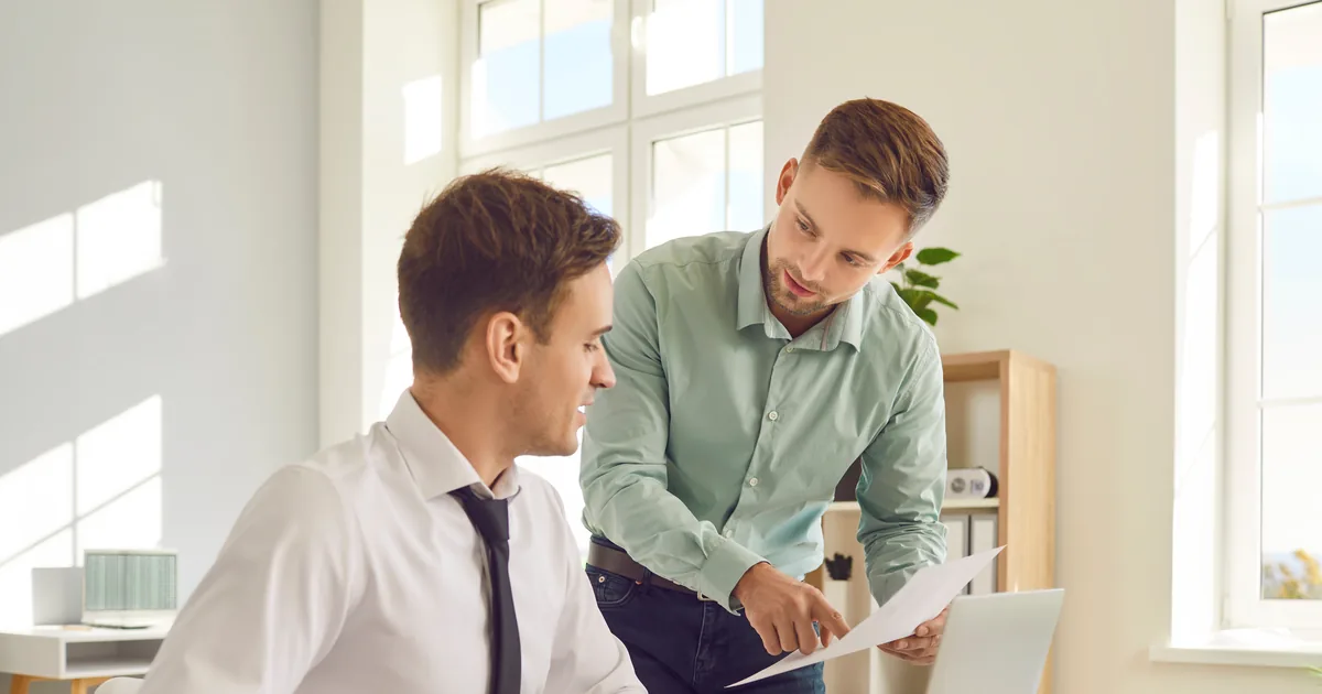 Two colleagues standing at a desk reviewing a document by a window