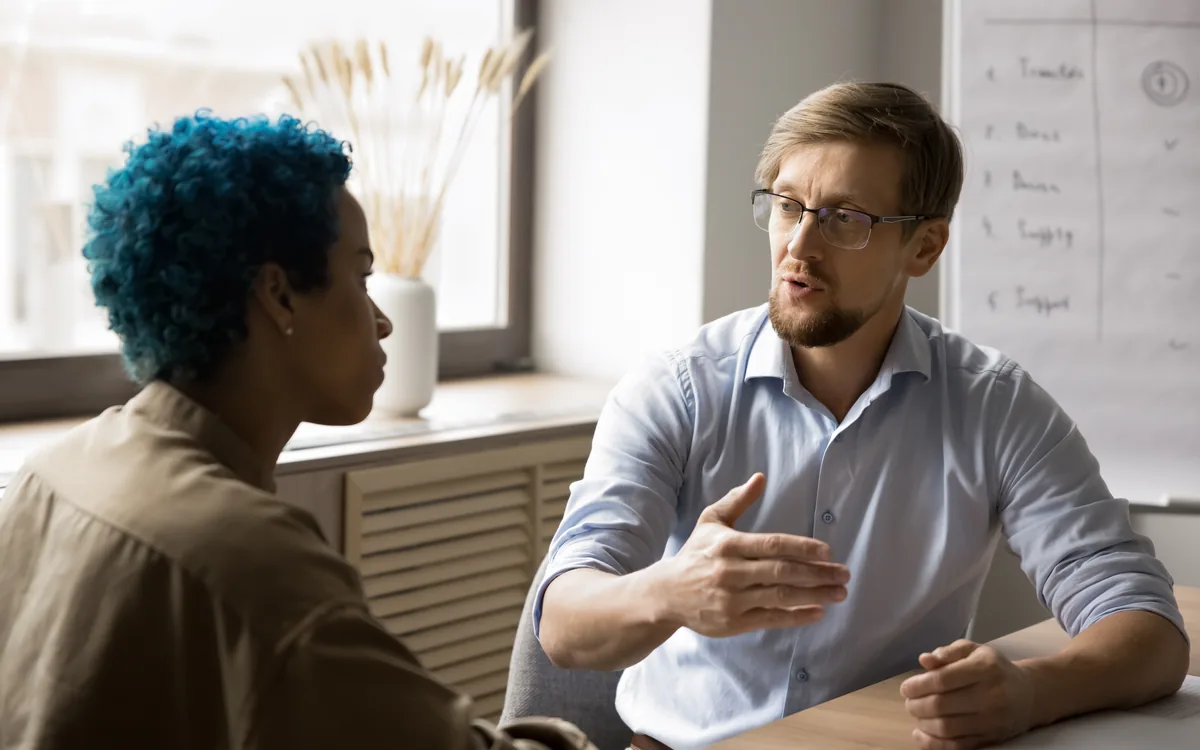 Two colleagues in conversation at a desk, one explaining a point