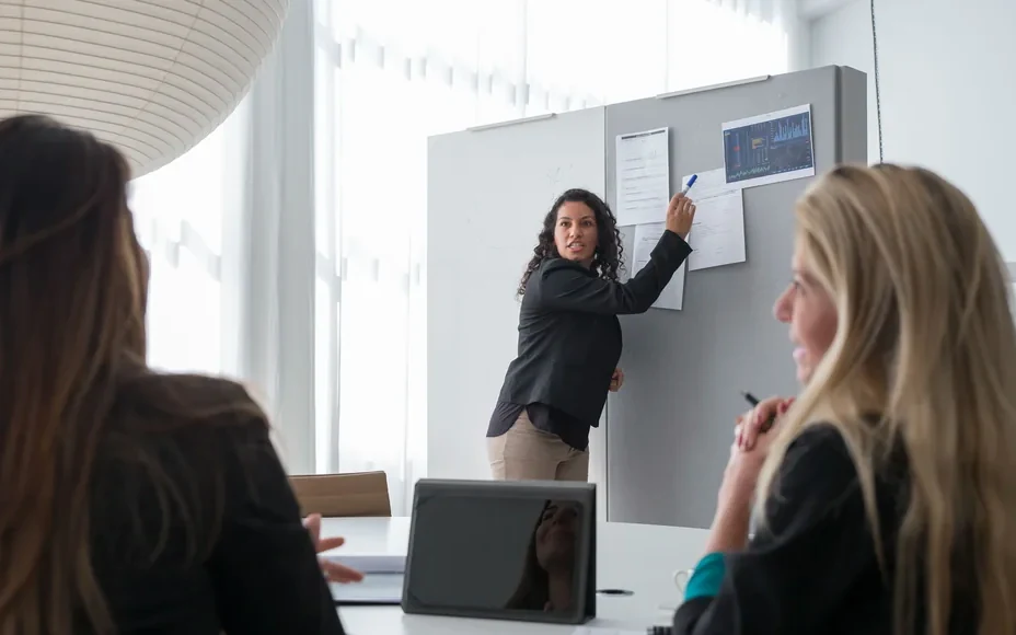A colleague briefing two others at a whiteboard in a meeting room